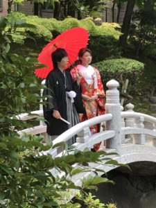 赤い傘をさして日本庭園の橋の上での着物のブライダルショット
