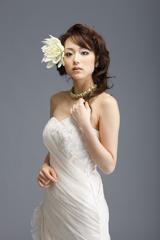 大きい花のヘッドドレスを付けたウェディングドレスを着るヘアメイクモデル
